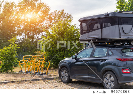 Modern SUV car campervan recreational motor home vehicle with rooftop tent bed parked at parking site near park or forest area. Motorhome campground stataion travel destination. RV lifestyle 94676868