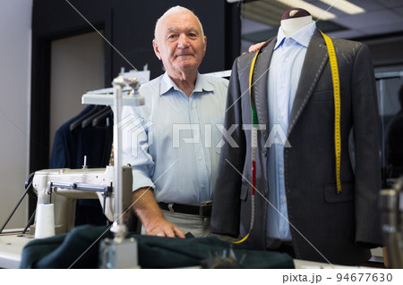 Experienced tailor tries on a new jacket on a mannequin in workshop 94677630