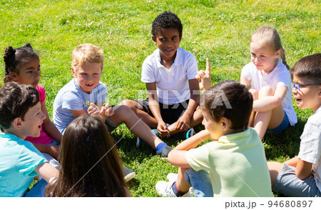 Group of happy kids resting on grass together and chatting in park Group of happy kids resting on grass together and chatting in park 94680897