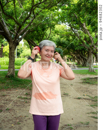 Portrait of happy senior adult elderly asia woman smiling standing and holding fresh vegetable and apple in the park. 94682302