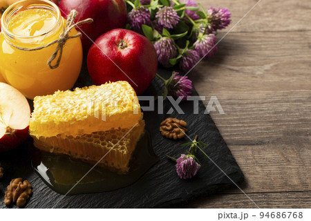 Mason jar with honey, honeycomb, red apples and walnuts on kitchen table 94686768