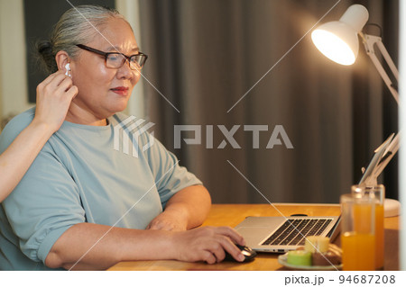 Grandson helping grandmother to put in earbuds when she is working on laptop 94687208