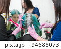 Process of hair dye in beauty salon. Two hairdressers in pink protective gloves applying paint to female hair during bleaching hair roots. 94688073