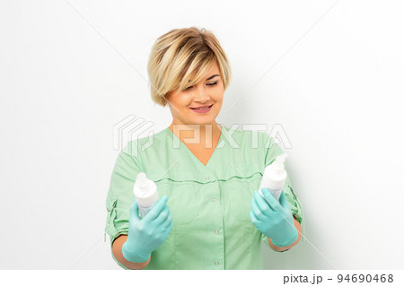 Cosmetics creams and skin care products in the hands of the female beautician smiling and standing over the white wall background 94690468