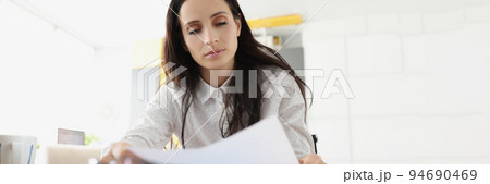 Tired overworked young woman go through paper on working place 94690469