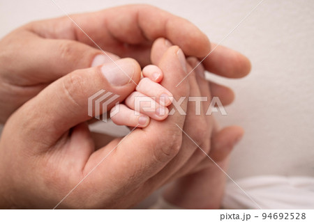 A newborn holds on to mom's, dad's finger. Hands of parents and baby close up. A child trusts and holds her tight. Tiny fingers of a newborn. The family is holding hands. Concepts of family and love. A newborn holds on to mom's, dad's finger. Hands of parents and baby close up. A child trusts and holds her tight. Tiny fingers of a newborn. The family is holding hands. Concepts of family and love. 94692528