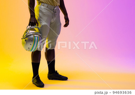 Midsection of african american male american football player with neon purple and yellow lighting Midsection of african american male american football player with neon purple and yellow lighting 94693636