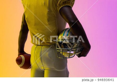 Midsection of african american male american football player with neon purple and yellow lighting Midsection of african american male american football player with neon purple and yellow lighting 94693641