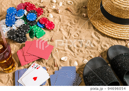 Beachpoker. Chips and cards on the sand. Around the seashells, hat and flip flops. Top view Beachpoker. Chips and cards on the sand. Around the seashells, hat and flip flops. Top view 94696054