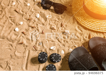 Beachpoker. Chips on the sand. Around the seashells, sunglasses and flip flops. Top view Beachpoker. Chips on the sand. Around the seashells, sunglasses and flip flops. Top view 94696075
