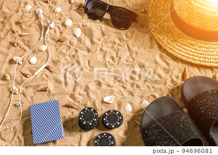 Beachpoker. Chips and cards on the sand. Around the seashells, sunglasses and flip flops. Top view Beachpoker. Chips and cards on the sand. Around the seashells, sunglasses and flip flops. Top view 94696081