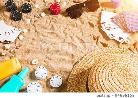 Beachpoker. Chips and cards on the sand. Around the seashells, sunglasses and hat. Top view 94696158