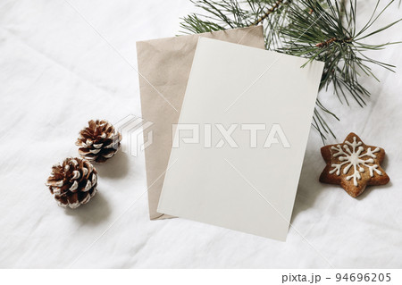 Christmas still life. Empty greeting card, invitation mockup. Gingerbread cookie, pine cones and pine tree branches on white linen tablecloth in sunlight. Gift wrapping concept. Winter festive flatlay Christmas still life. Empty greeting card, invitation mockup. Gingerbread cookie, pine cones and pine tree branches on white linen tablecloth in sunlight. Gift wrapping concept. Winter festive flatlay 94696205