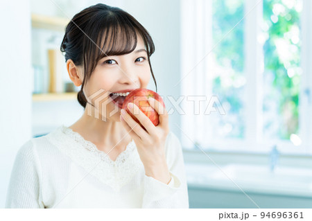 キッチンでリンゴを食べる若い女性 キッチンでリンゴを食べる若い女性 94696361