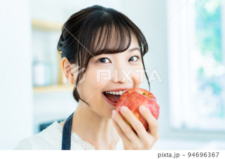 キッチンでリンゴを食べる若い女性 キッチンでリンゴを食べる若い女性 94696367