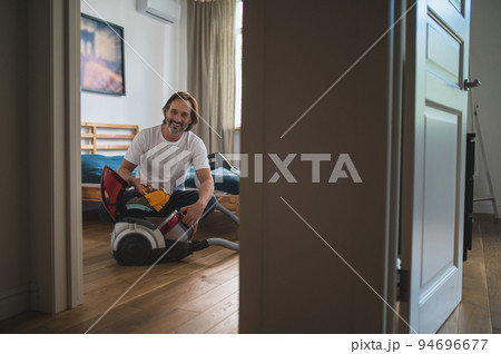 Man sitting on the floor and gathering the vacuum cleaner 94696677