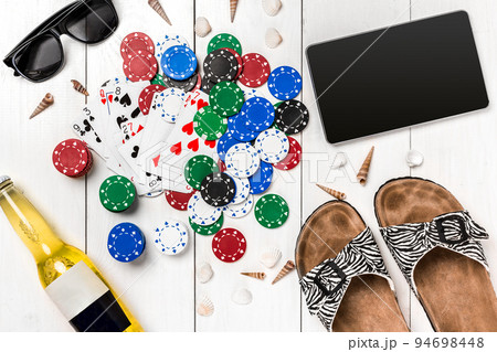 Card deck surrounded by poker chips and scattered seashells on white wooden background with copy space 94698448