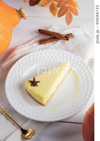 Autumn cozy image with pumpkin pie piece on white plate on napkin on white wooden table. Halloween or Thanksgiving concept. Fall holidays sweet seasonal food. Vertical orientation. Selective focus. Autumn cozy image with pumpkin pie piece on white plate on napkin on white wooden table. Halloween or Thanksgiving concept. Fall holidays sweet seasonal food. Vertical orientation. Selective focus. 94698735