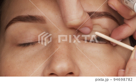 Woman on modern eyelash lamination procedure in a professional beauty salon. Master applies special glue before the eyelash curling procedure, close up. Beauty salon.. Woman on modern eyelash lamination procedure in a professional beauty salon. Master applies special glue before the eyelash curling procedure, close up. Beauty salon.. 94698782