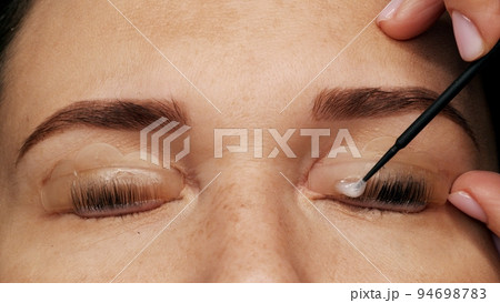Woman on modern eyelash lamination procedure in a professional beauty salon. Master applies special glue before the eyelash curling procedure, close up. Beauty salon.. Woman on modern eyelash lamination procedure in a professional beauty salon. Master applies special glue before the eyelash curling procedure, close up. Beauty salon.. 94698783