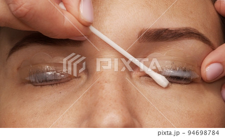 Woman face on modern eyelash lamination procedure in a professional beauty salon. Master applies special glue before the eyelash curling procedure, close up. Beauty salon.. 94698784