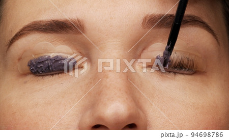 Woman face on modern eyelash lamination procedure in a professional beauty salon. Master applies special glue before the eyelash curling procedure, close up. Beauty salon.. 94698786