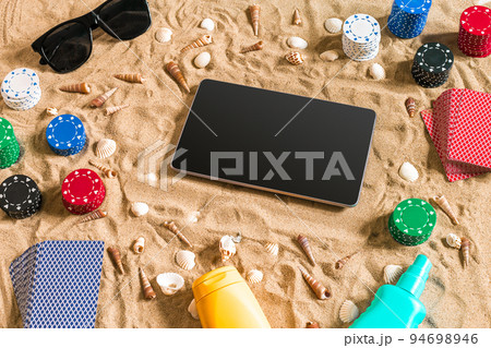 Gambling on vacation concept - white sand with seashells , colored poker chips and cards. Top view Gambling on vacation concept - white sand with seashells , colored poker chips and cards. Top view 94698946