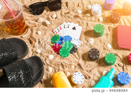 Beachpoker. Chips and cards on the sand. Around the seashells, sunglasses and flip flops. Top view 94698984