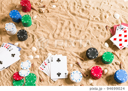 Beachpoker. Chips and cards on the sand with seashells. Top view Beachpoker. Chips and cards on the sand with seashells. Top view 94699024