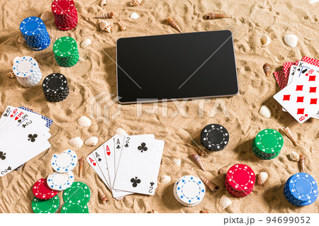 Gambling on vacation concept - white sand with seashells , colored poker chips and cards. Top view Gambling on vacation concept - white sand with seashells , colored poker chips and cards. Top view 94699052