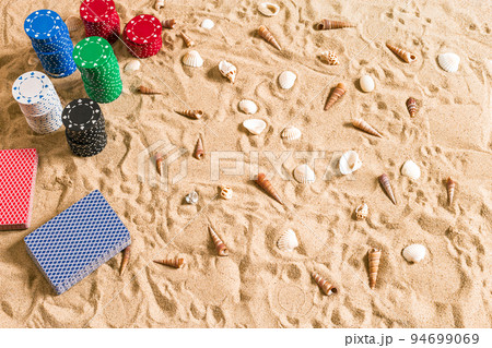 Beachpoker. Chips and cards on the sand with seashells. Top view Beachpoker. Chips and cards on the sand with seashells. Top view 94699069
