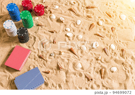 Beachpoker. Chips and cards on the sand with seashells. Top view Beachpoker. Chips and cards on the sand with seashells. Top view 94699072