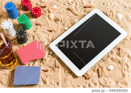 Online poker game on the beach with digital tablet and stacks of chips. Top view 94699080