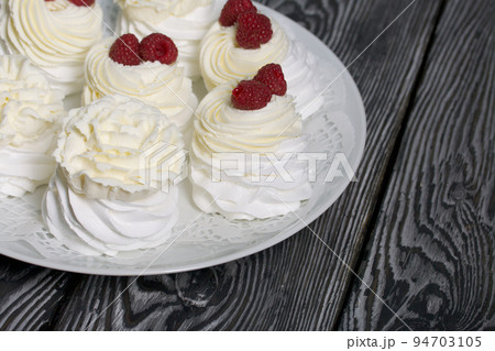 Cake Anna Pavlova, meringue and cream. Garnished with raspberries. Lying on a platter, close-up. 94703105