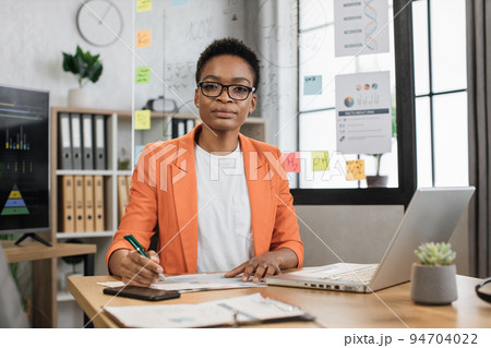 African american business lady using wireless laptop and taking notes while working at office room. African american business lady using wireless laptop and taking notes while working at office room. 94704022