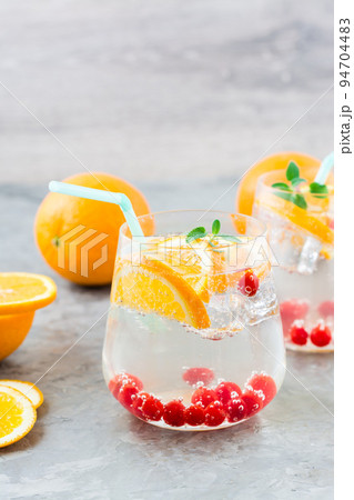 Hard seltzer cocktail with orange, cranberry and mint in glasses on the table. Alcoholic beverage. Vertical view 94704483