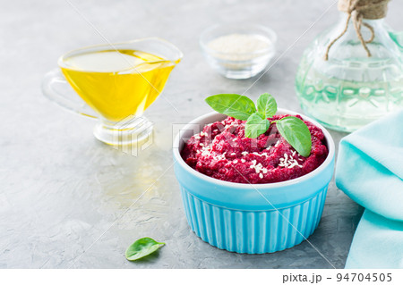 Baked beet hummus in a bowl with sesame seeds and basil on the table. Close-up 94704505