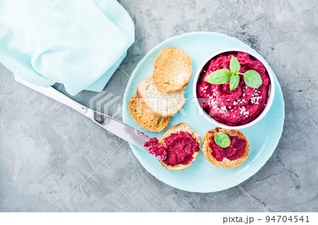 Homemade bruschetta with beetroot hummus on small toast on a plate and a table knife on the table. Top view 94704541