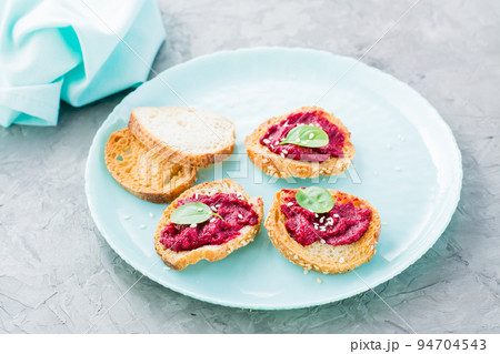 Homemade bruschetta with beetroot hummus on small baked baguette toast on a plate on the table. Close-up Homemade bruschetta with beetroot hummus on small baked baguette toast on a plate on the table. Close-up 94704543