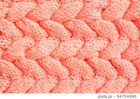 Textured background. Knitted fabric in peach color in the form of intertwined braids. Top view Textured background. Knitted fabric in peach color in the form of intertwined braids. Top view 94704990