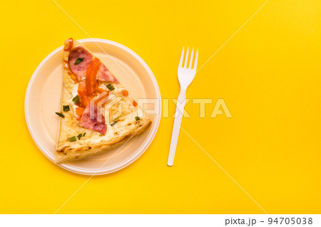 Takeaway and delivery. Pizza slice in disposable plastic plate and fork on yellow background Takeaway and delivery. Pizza slice in disposable plastic plate and fork on yellow background 94705038