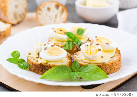 Hearty breakfast in the morning. Fresh baguette sandwiches with butter, quail eggs, flax seeds and basil seeds on a plate. Close-up 94705087