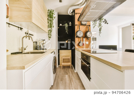 Fragment of interior of light narrow home kitchen with minimalist style white furniture with sink and stove 94706426