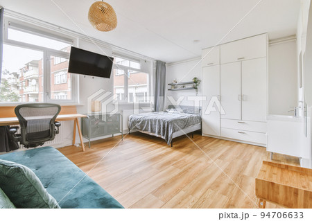 Home interior design of bedroom with bed and wooden wardrobe placed in corner near window in modern apartment 94706633