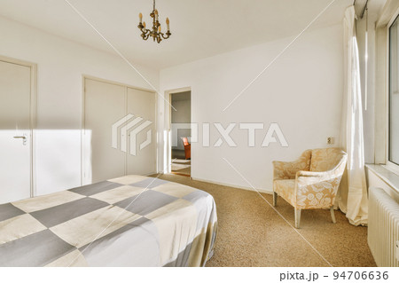 Comfortable bed with white bedclothes and bedside table with lamp placed near window and balcony door in light bedroom at home Comfortable bed with white bedclothes and bedside table with lamp placed near window and balcony door in light bedroom at home 94706636