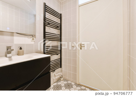 Sinks with mirrors and clean bathtub located near shower box with glass door in modern bathroom with white tiled walls Sinks with mirrors and clean bathtub located near shower box with glass door in modern bathroom with white tiled walls 94706777