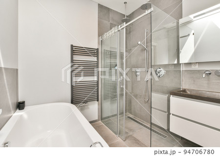 Sinks with mirrors and clean bathtub located near shower box with glass door in modern bathroom with white tiled walls Sinks with mirrors and clean bathtub located near shower box with glass door in modern bathroom with white tiled walls 94706780
