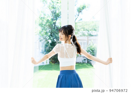 カーテンを開けて日差しを浴びる若い女性 94706972