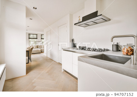 Contemporary minimalist style interior design of light studio apartment with wooden table and chairs in dining zone between open kitchen and living room with white walls and parquet floor 94707152