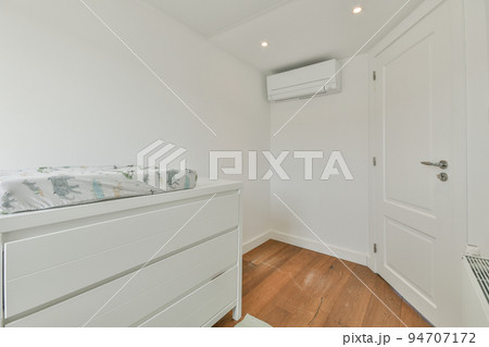 Interior of white room with baby crib and armchair near window with blue chest of drawers in daylight 94707172